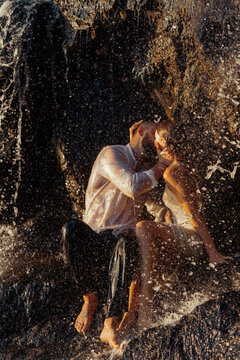 Passionate couple kissing behind waterfall spray in warm sunset light
