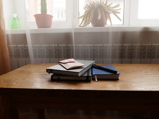 Books, notebooks and a pen rest on a wooden table by the window, creating a cozy setting for studying and reading. © Vasyl
