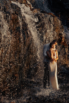 Romantic couple standing under waterfall spray in sunset light