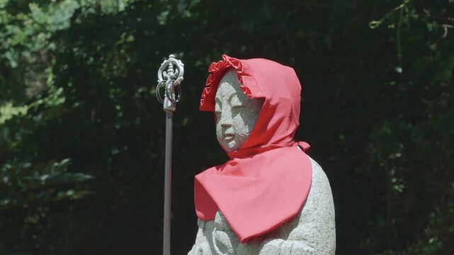Japanese stone Buddhist statue wearing a red hood in a forest