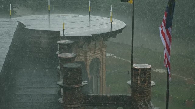 Heavy rain falling on Kellie's Castle rooftop, wet historical brick architecture and Malaysian flag during tropical monsoon, weather conditions in Perak. Ipoh, Malaysia, 16 Nov 2025