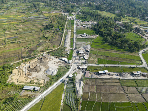 Aerial view of a stone crusher facility situated amidst lush green rice fields and agricultural land in Kecamatan Karangnongko, Jawa Tengah, Indonesia.