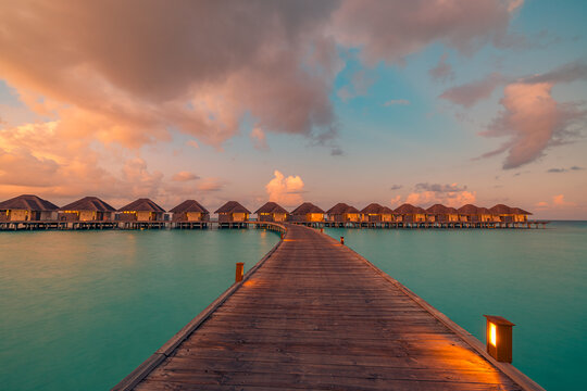 Romantic Maldives overwater villas wooden pier lights under colorful sunset sky glowing tropical ocean lagoon. Perfect summer travel landscape paradise. Luxury honeymoon getaway vacation wall art