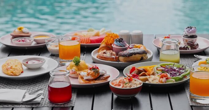 Gourmet breakfast selection with eggs benedict, pastries, fresh juices arranged on table, luxury resort poolside, tropical vacation dining background, high-end hotel breakfast service