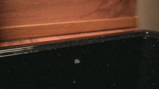 Close-up view of hand cleaning worn black suitcase edge with red sponge, visible sponge compression, firm scrubbing motion, scuffs, grime, and warm light revealing texture and travel wear