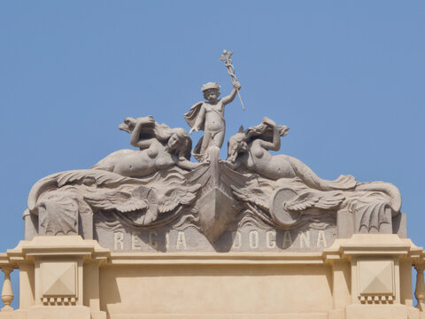 Sculptural relief pediment on the Regia Dogana historic customs house building featuring mermaids and child figure with caduceus staff in Messina, Sicily, Italy.
