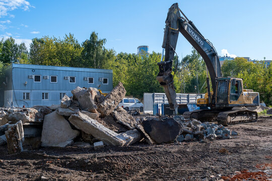 SAINT PETERSBURG, RUSSIA - AUGUST 11, 2026: Volvo tracked excavator with hydraulic breaker working at an urban demolition site, surrounded by large pieces of demolished concrete 