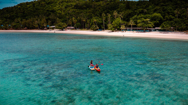 Group of tourist are enjoy on water sport paddle sup-board with kayaking along at the edge of the sea beach under crystal clear of water in the island of summer trip