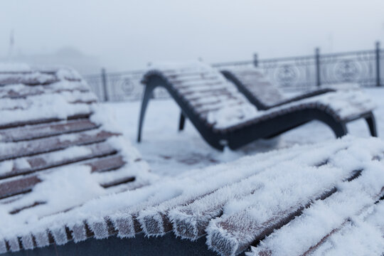 Wooden sunbeds covered with thick hoarfrost on the winter embankment in Arkhangelsk during foggy weather.