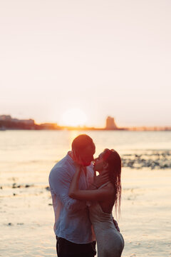 Full length passionate couple embracing in water about to kiss at sunset, young man and woman on river shore