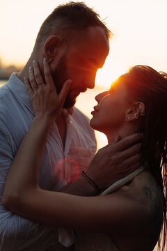 Romantic couple embracing at sunset, young lovers touching faces tenderly in golden sunlight