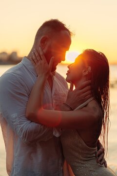 Romantic couple embracing at sunset, young lovers touching faces tenderly in golden sunlight
