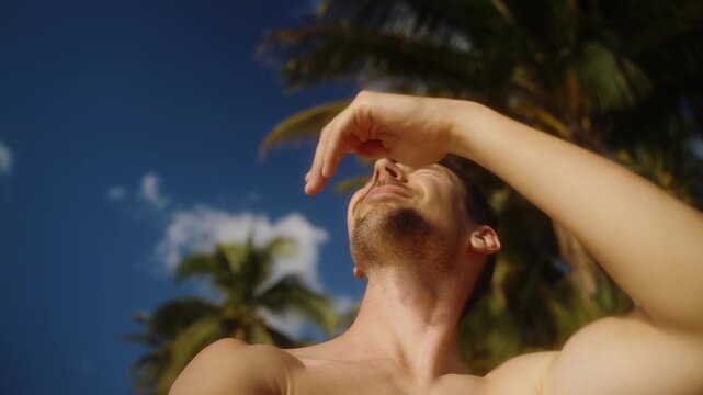 Tourist making selfie video under palm trees at the beach. He shields his eyes from sunlight, summer vacation and travel lifestyle.