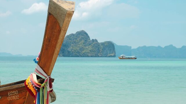 Longtail boat prow decorated with colorful sashes floating near turquoise water, limestone island background in Andaman Sea, tropical Thailand travel destination advertisement
