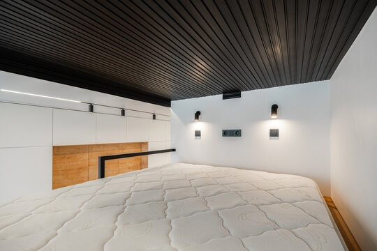 Mattress on mezzanine floor with black slatted ceiling
