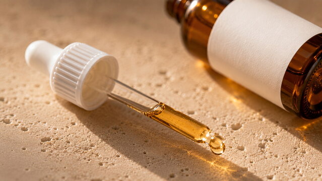Extreme macro close-up of a detached cosmetic glass dropper filled with golden facial oil beside an amber skincare bottle on warm beige limestone, illuminated by soft natural sunlight.