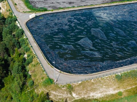 Aerial view of a sewage sludge storage basin covered with a black membrane for odor control, situated near a forest in Riga, Latvia.