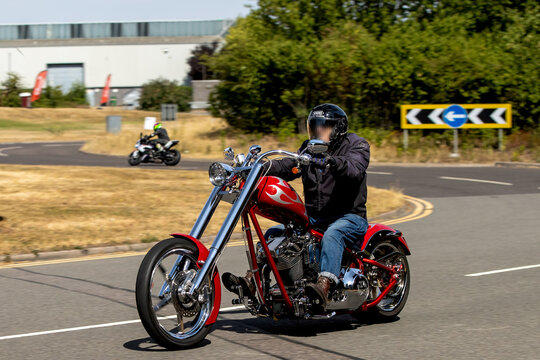 Milton Keynes,UK - Aug 2nd 2026:  Man riding a red Big Bear Choppers Sled Chopper chassis configuration chopper-style motorcycle motorcycle driving on a British road
