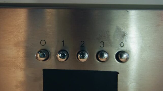 Front view of stainless steel control panel featuring five round metal push buttons numbered 0 through 4, with brushed surface texture, visible wear marks, bright reflections, and dark rectangular