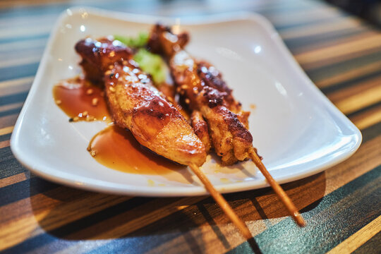 Chicken yakitori skewers glazed with teriyaki sauce on a white plate