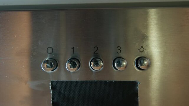 Frontal close-up of brushed stainless steel control panel showing row of four numbered circular push buttons with indicator lights above each button and dark vent opening at lower edge