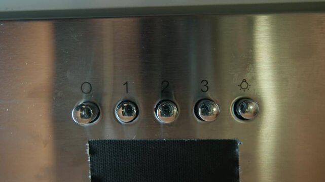 Close frontal view of stainless steel control panel with five circular numbered push buttons, index finger pressing button one, brushed metal surface showing smudges, fingerprints, light scratches