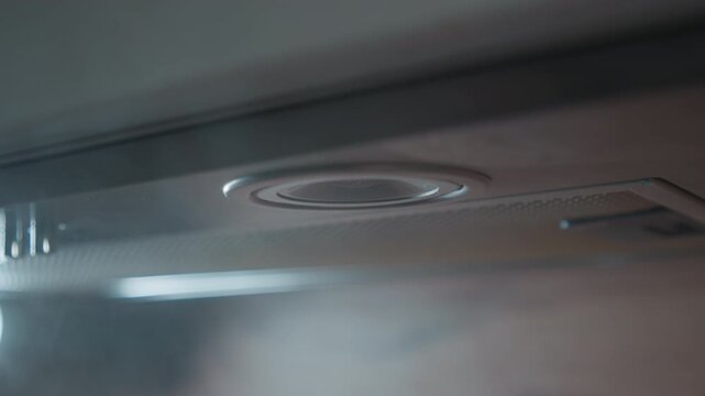 Low angle interior scene with recessed circular ceiling vent beside rectangular control panel, while diffuse steam drifts forward and gently disperses through cool neutral light and soft shadows