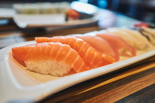Row of salmon nigiri sushi on a white plate from an angle