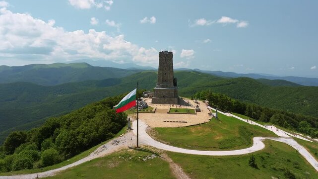 Shipka Freedom Monument aerial drone view waving Bulgarian national flag green Balkan mountain ranges background historical landmark summer Bulgaria travel