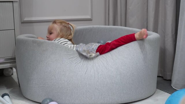 Energetic toddler enjoys playful activity, climbing into soft indoor ball pit filled with colorful spheres for joyful childhood exploration