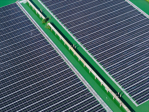 Aerial view of a floating solar power plant with photovoltaic panels mounted on pontoons over green wastewater treatment ponds in Latvia.