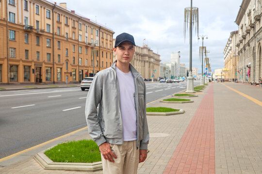 Young man in light clothes and black cap standing on wide city street enjoying urban lifestyle casual fashion during summer day outdoors.