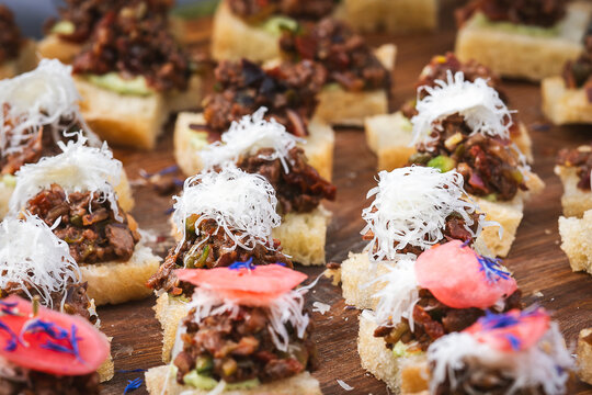 Cormorant breast tartare served as bite-sized canap&eacute;s on bread on Kihnu Island, Estonia, topped with grated garnish, pickled radis and edible flowers, presenting an unconventional wild food creation.