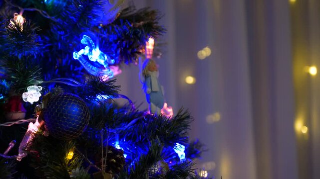 Twinkling blue LED light and festive ornament on Christmas tree branch create cozy holiday atmosphere.