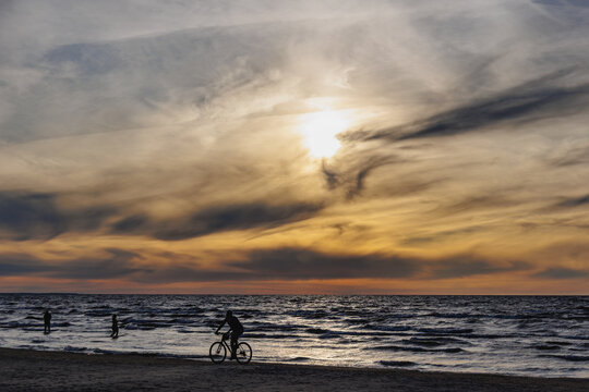 Silhouette of cyclist riding bicycle on sandy beach during sunset in Majori, Jurmala, Latvia