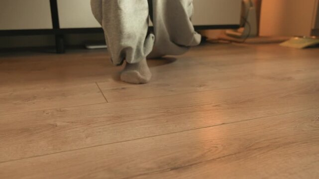 Close low-angle view of electronic keyboard with hands pressing keys and bare feet on wooden floor, capturing visible playing motion and subtle weight shifts during relaxed home practice