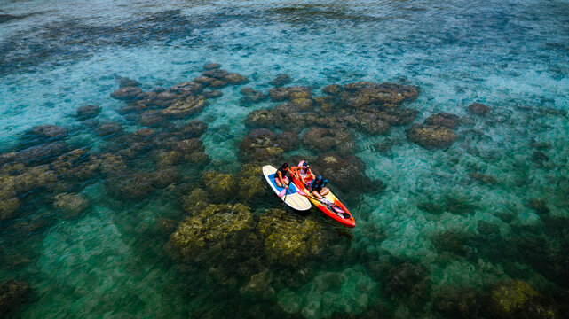 Top aerial view of Group of tourist are enjoy on water sport paddle sup-board with kayaking along at the edge of the sea beach under crystal clear of water in the island of summer trip