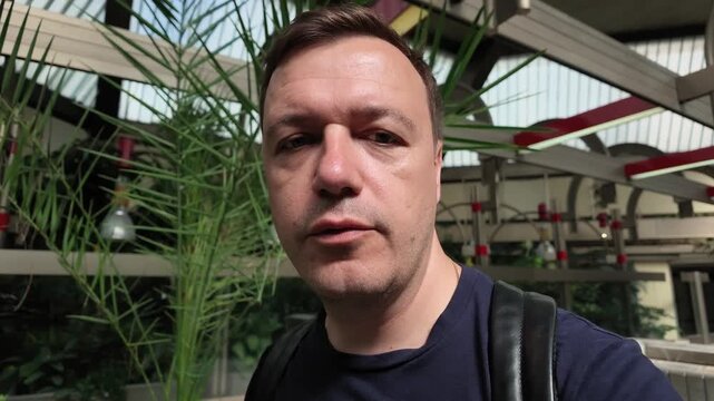 Man recording vlog in modern greenhouse atrium while talking to camera lens about his botanical surroundings