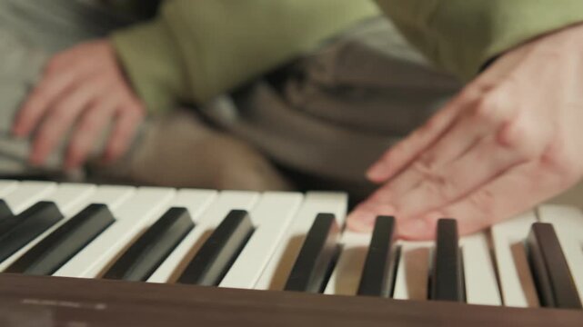 Low-angle view of hands actively playing piano keys with visible finger motion, pressed notes, glossy black and white keyboard, and focused performance energy in warm indoor setting