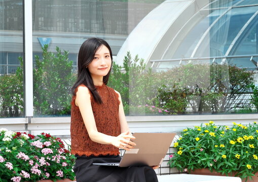 屋外テラスのベンチでノートパソコンを開き仕事をする若い女性