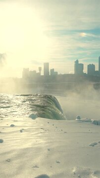Winter Niagara Falls view with rising mist, snowy riverbank and Skylon Tower skyline