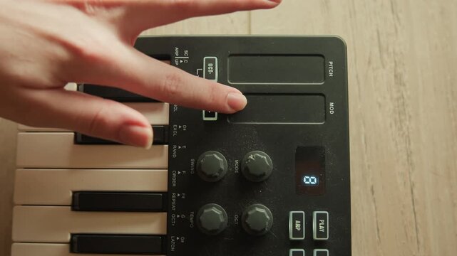 Top-down close-up shows left section of compact electronic keyboard while hand presses and slides touch strip beside rotary knobs, creating visible pitch and modulation changes in music setup
