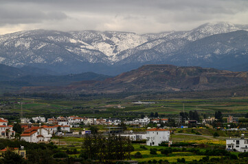 Obraz premium Majestic mountains cradle a tranquil village under a cloudy sky in early spring