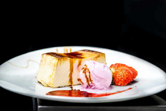 Basque cheesecake slice with raspberry ice cream, strawberry, and fruit jam drizzle