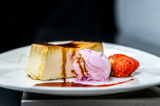 Cheesecake slice with raspberry ice cream, caramel sauce, and fresh strawberry