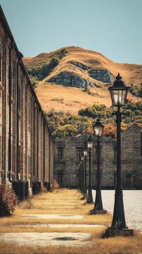 A walkway lined with old brick buildings and vintage street lamps under a hill.