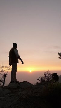 Silhouette of a Man Walking Toward and Watching the Sunset from a Hilltop, Peaceful Golden Hour Landscape in the Mountains