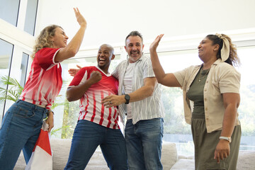 Obraz premium Diverse friends wearing striped red-and-white jerseys celebrating in living room, waving scarf