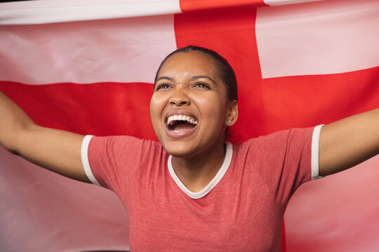 African woman cheering holding red white cross flag in studio wearing ringer tee and stud earring