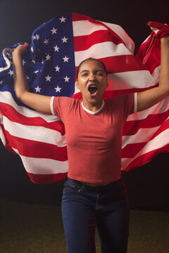 Adult African American woman holding US flag, shouting in studio wearing red ringer tee
